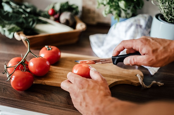 Person schneidet mit einem scharfen Messer die runde Tomate auf dem Holzbrett