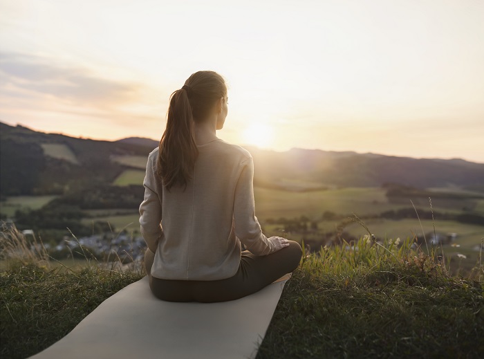 Eine Frau sitzt auf einer Yogamatte und schaut in den Sonnenaufgang