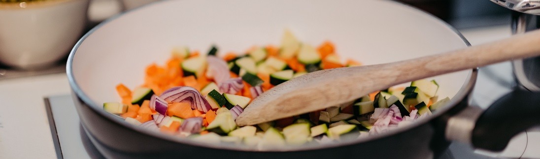 Kleingeschnittenes Gemüse wird in einer Pfanne zubereitet.