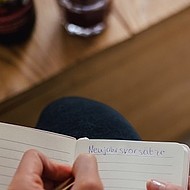 Jemand schreibt in ein Notizbuch, der Text "Neujahrsvorsätze" ist zu erkennen.