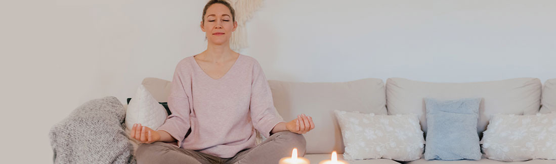 Frau sitzt als Tipp gegen Stress in Mediationspose auf dem Sofa